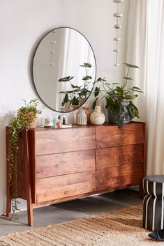 a wooden dresser topped with plants and a round mirror