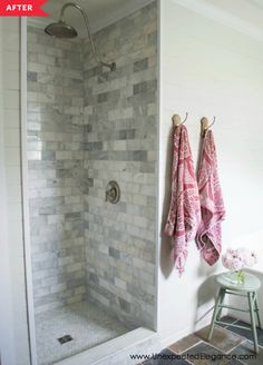 a walk in shower with two towels hanging on the wall and a stool next to it