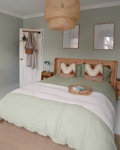 a bed with green sheets and pillows in a bedroom next to a white door that has pictures on the wall above it