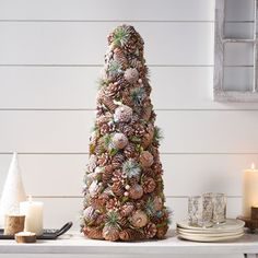 a pine cone christmas tree sitting on top of a table next to candles and plates