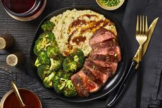 steak, mashed potatoes and broccoli on a black plate with silverware