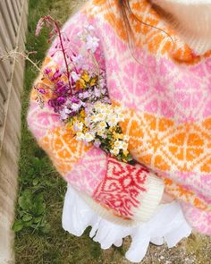 a woman wearing a colorful sweater holding flowers