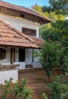 a white house with a brown roof and red tile on it's side, surrounded by greenery