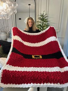 a woman is holding up a red and white knitted blanket with santa's belt on it