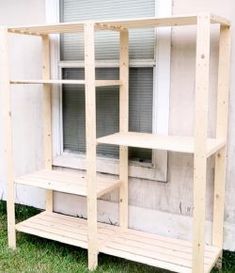 a wooden shelf sitting in the grass next to a window