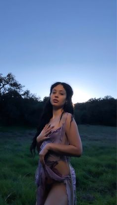 a woman is standing in the grass at sunset