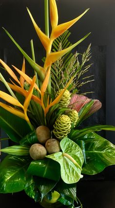 an arrangement of tropical plants and flowers in a vase on a black table with green leaves