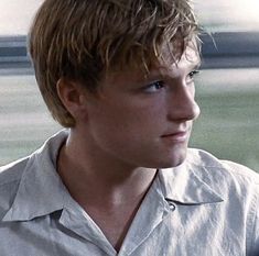 a young man with blonde hair wearing a white shirt and looking off into the distance