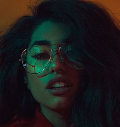 a woman wearing glasses with green light on her face and long dark hair in the background