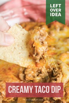 a hand holding a tortilla chip over a bowl of creamy taco dip