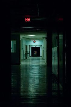 an empty hallway in the dark with a red sign on the exit door that says fii