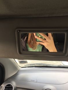 a woman's reflection in the rear view mirror of a car, with her hand up to her face