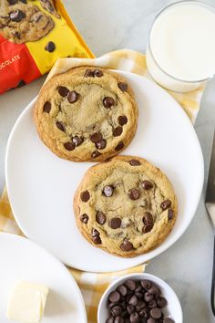 two chocolate chip cookies sitting on top of a white plate next to a cup of milk