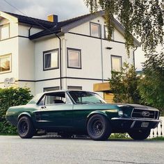 an old green mustang parked in front of a white house on the side of the road