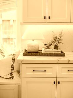 a kitchen with white cupboards and a lamp on top of the cabinet door, in front of a window