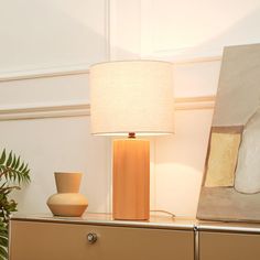 a table lamp sitting on top of a dresser next to a painting and potted plant