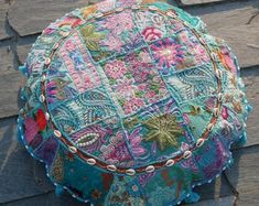 a multicolored patchwork round pillow sitting on top of a wooden floor next to a brick wall