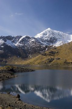 the mountains are covered in snow and there is a small lake on the ground near it