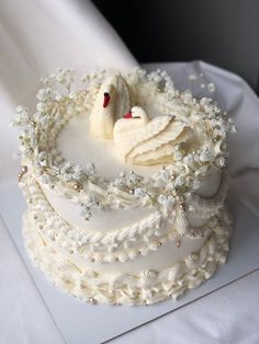 a wedding cake with two swans on top and white frosting flowers around the edges