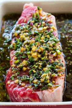 a piece of raw meat with herbs on top in a red casserole dish