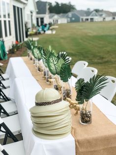 a long table topped with lots of white plates and vases filled with palm leaves