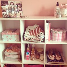 a book shelf filled with lots of books and other items next to a pink wall