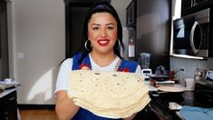 a woman holding up a tortilla in her kitchen