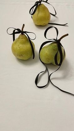 three pears tied up with black ribbon on white surface, one has two green apples and the other is brown