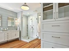 a large bathroom with wooden floors and white cabinetry on the wall, along with a walk in shower