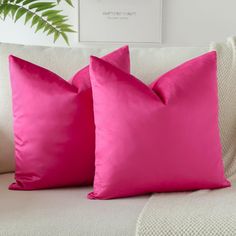 two pink pillows sitting on top of a white couch