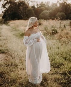 a woman in a white dress is walking through the grass with her hands on her hips