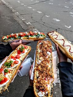 four people holding long sandwiches with toppings on them in front of a street corner