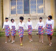 a group of women in white shirts and multicolored skirts are holding hands with each other