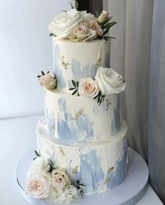 a three tiered cake with white and blue flowers on the top, sitting on a table