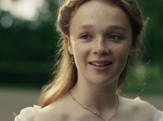 a woman with freckled hair and blue eyes wearing a white dress smiling at the camera