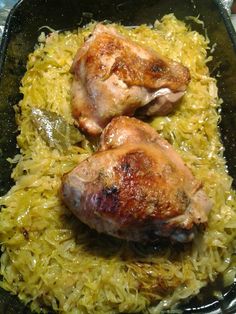 two pieces of chicken sitting on top of yellow rice in a black pan with spoons