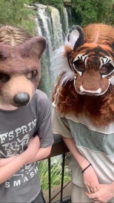 two people wearing animal masks next to a waterfall