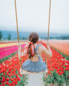 a woman sitting on a swing in a field full of tulips and flowers