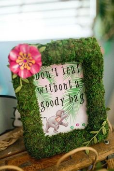 a moss covered frame with an elephant and flower on the top is sitting on a wooden table