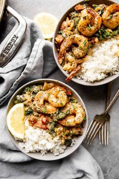 two bowls filled with shrimp and rice on top of a gray table next to silverware