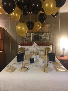 a bed topped with lots of black and gold balloons next to boxes on top of it