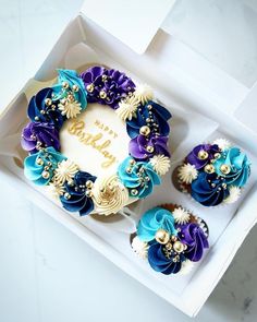 two cupcakes in a white box with blue and purple decorations