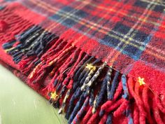 a red, blue and yellow plaid blanket with stars on the edge is laying on a green surface