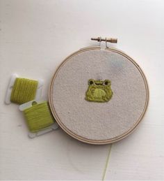 an embroidered frog is sitting next to two spools of thread