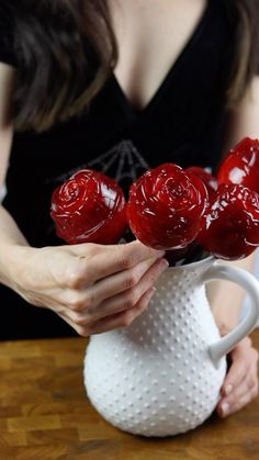 a woman is holding three red roses in a white vase on a table with a wooden surface