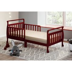 a baby crib with a stuffed animal next to it on a rug in front of a window