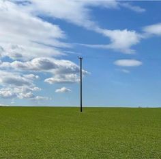 an empty field with a telephone pole in the distance and clouds in the sky above