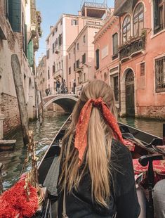 a woman riding on the back of a boat down a canal