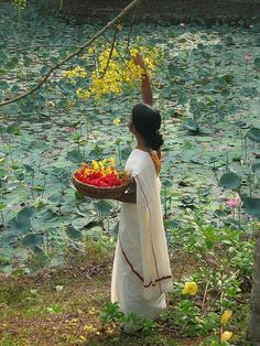 a woman holding a basket full of flowers in front of water lillies and trees