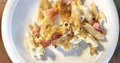 a white plate topped with pasta covered in cheese and bacon next to a silver fork